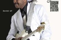 Musician in white outfit and hat holding a guitar with album title "raise up" by larry graham & graham central station.