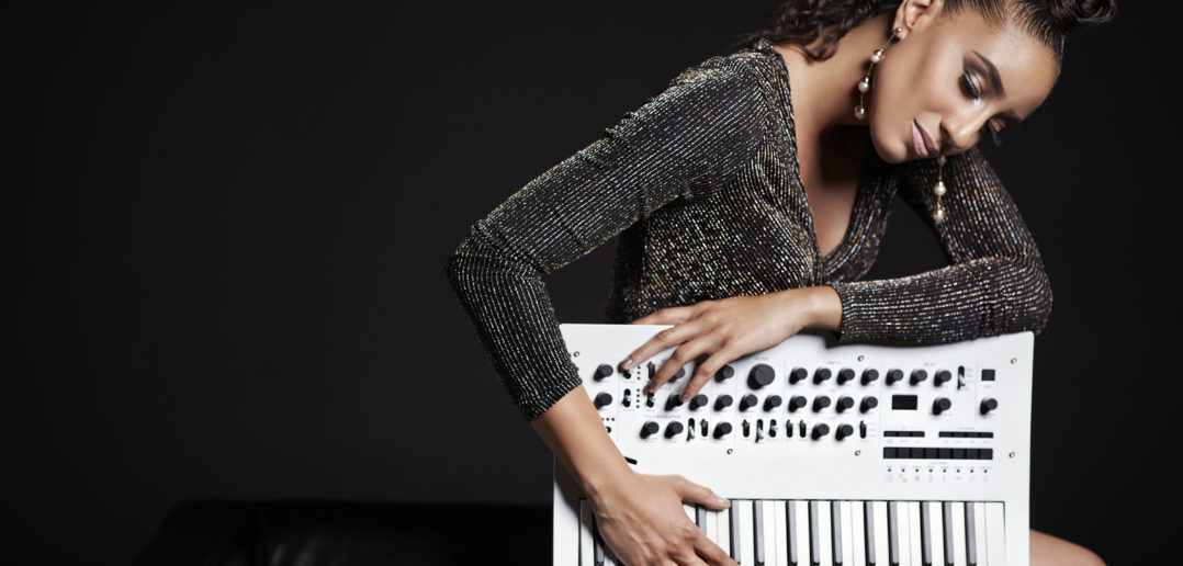 Fashionable woman posing with a synthesizer against a dark background.