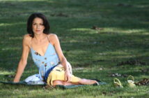 A woman in a blue and yellow dress sitting on the grass.